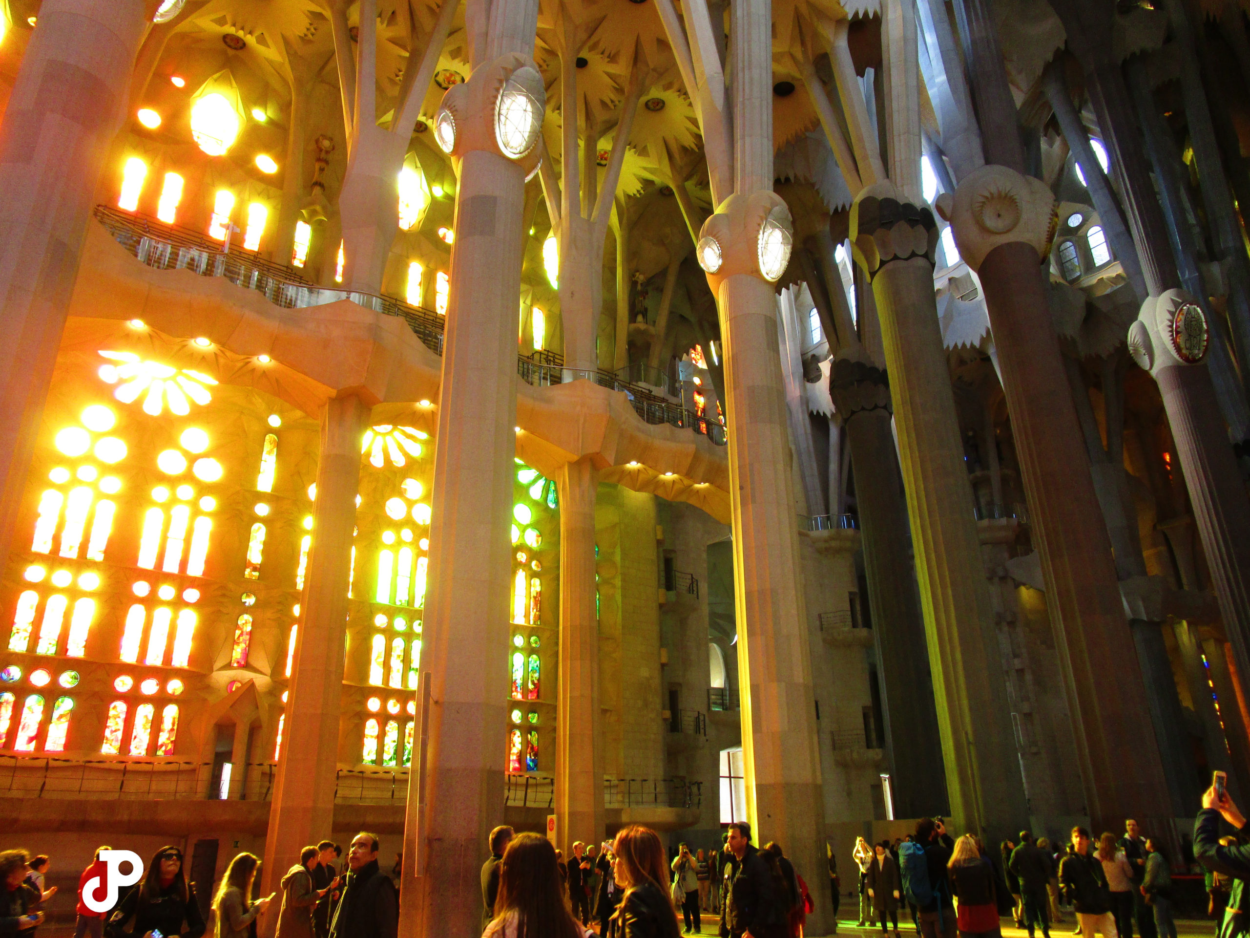 sunlight filtering through the colorful stained glass windows of La Sagrada Familia, washing the interior in bright orange light