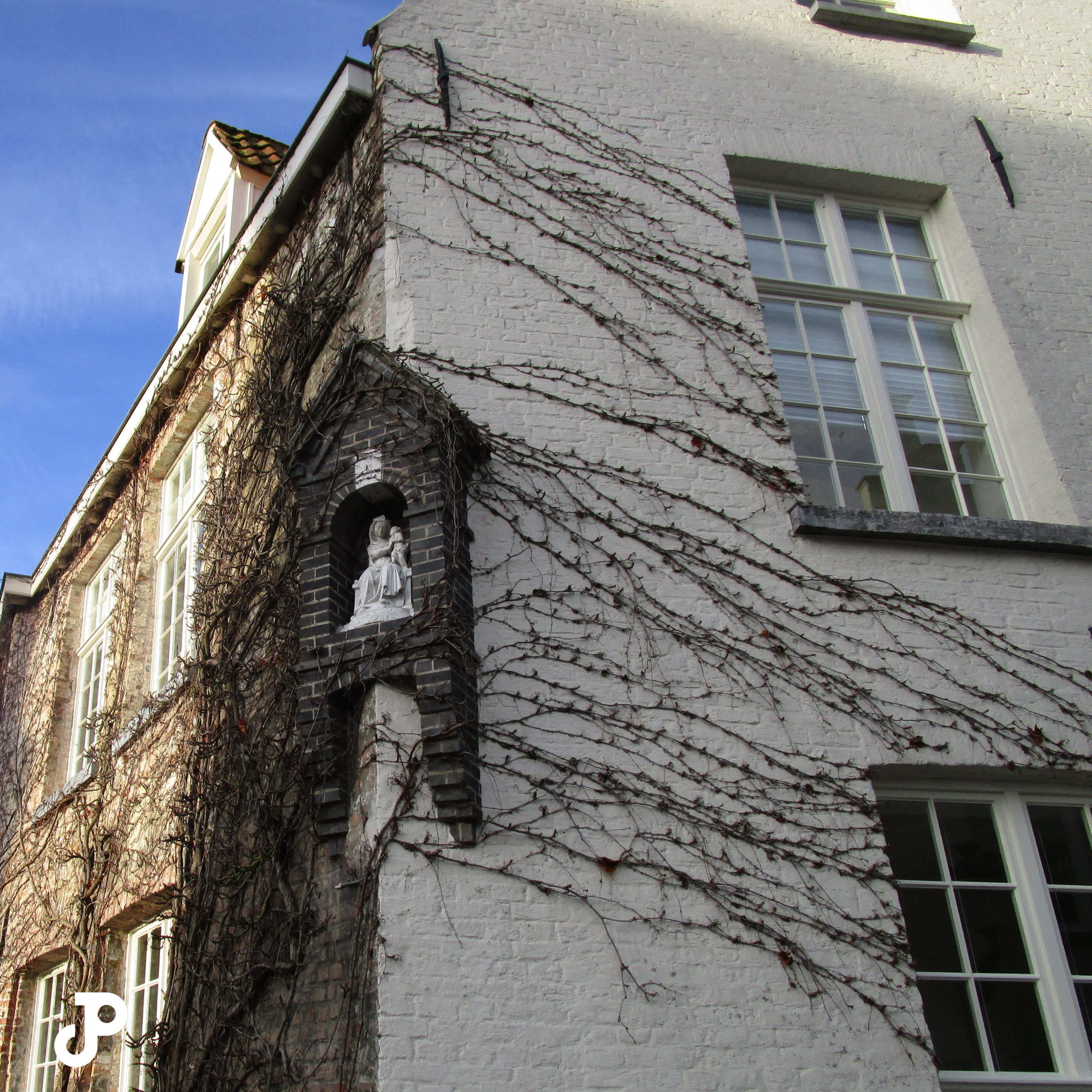 a building covered in ivy shoots, surrounding a statue of the Virgin Mary and Jesus inset into the wall