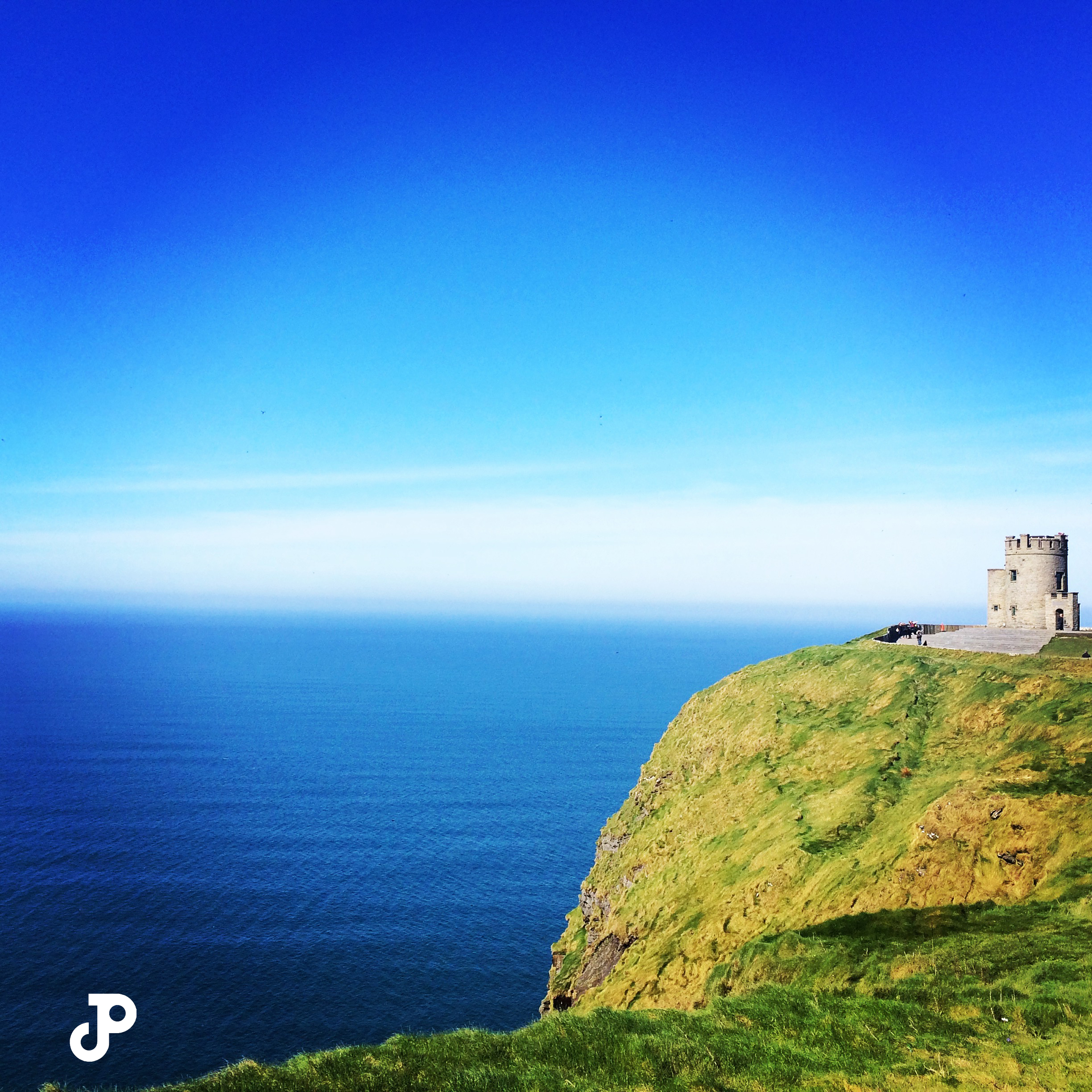 a small castle perched on a grassy cliff overlooking the sea on a bright, clear day