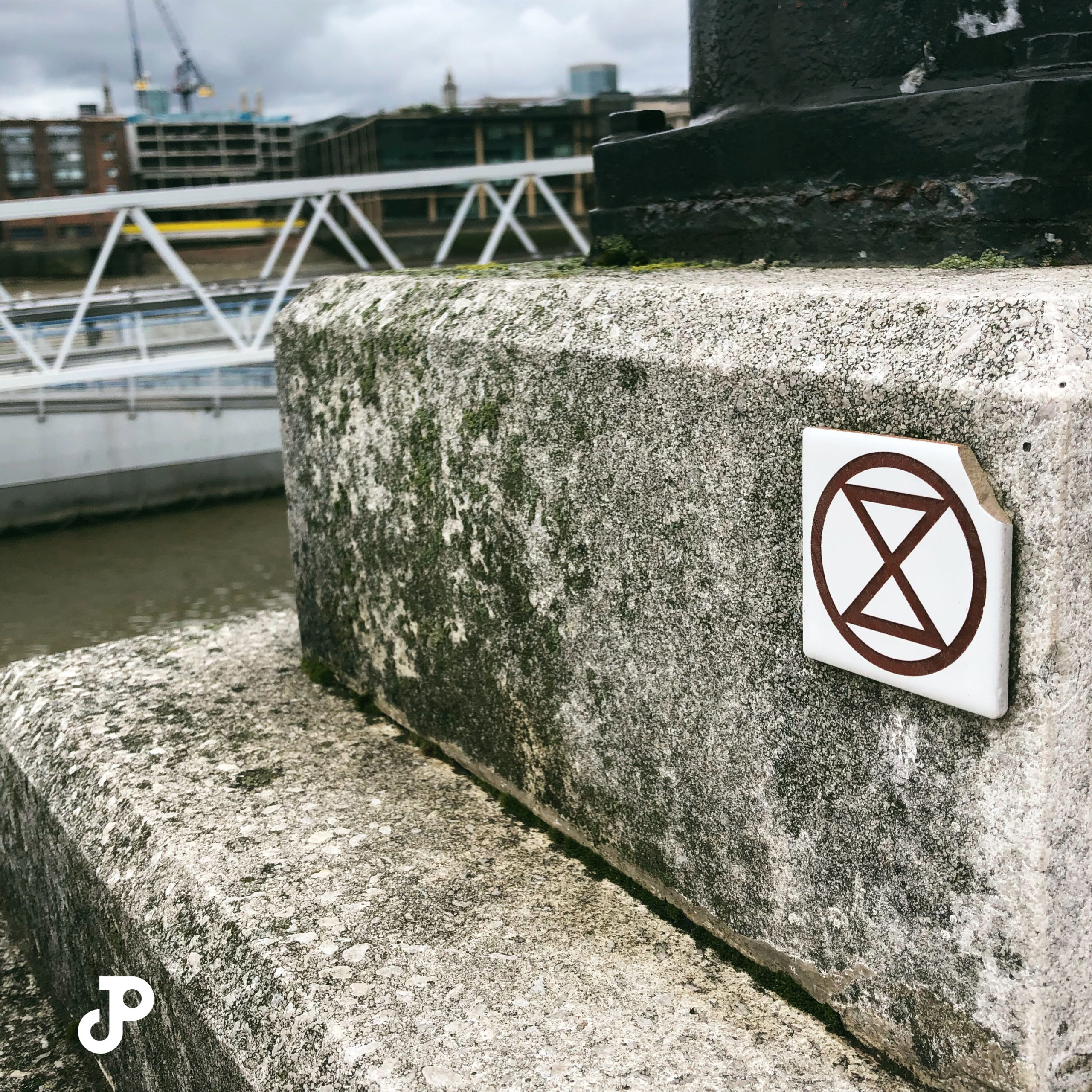 a small tile on a concrete slab, showing the Extinction Rebellion logo