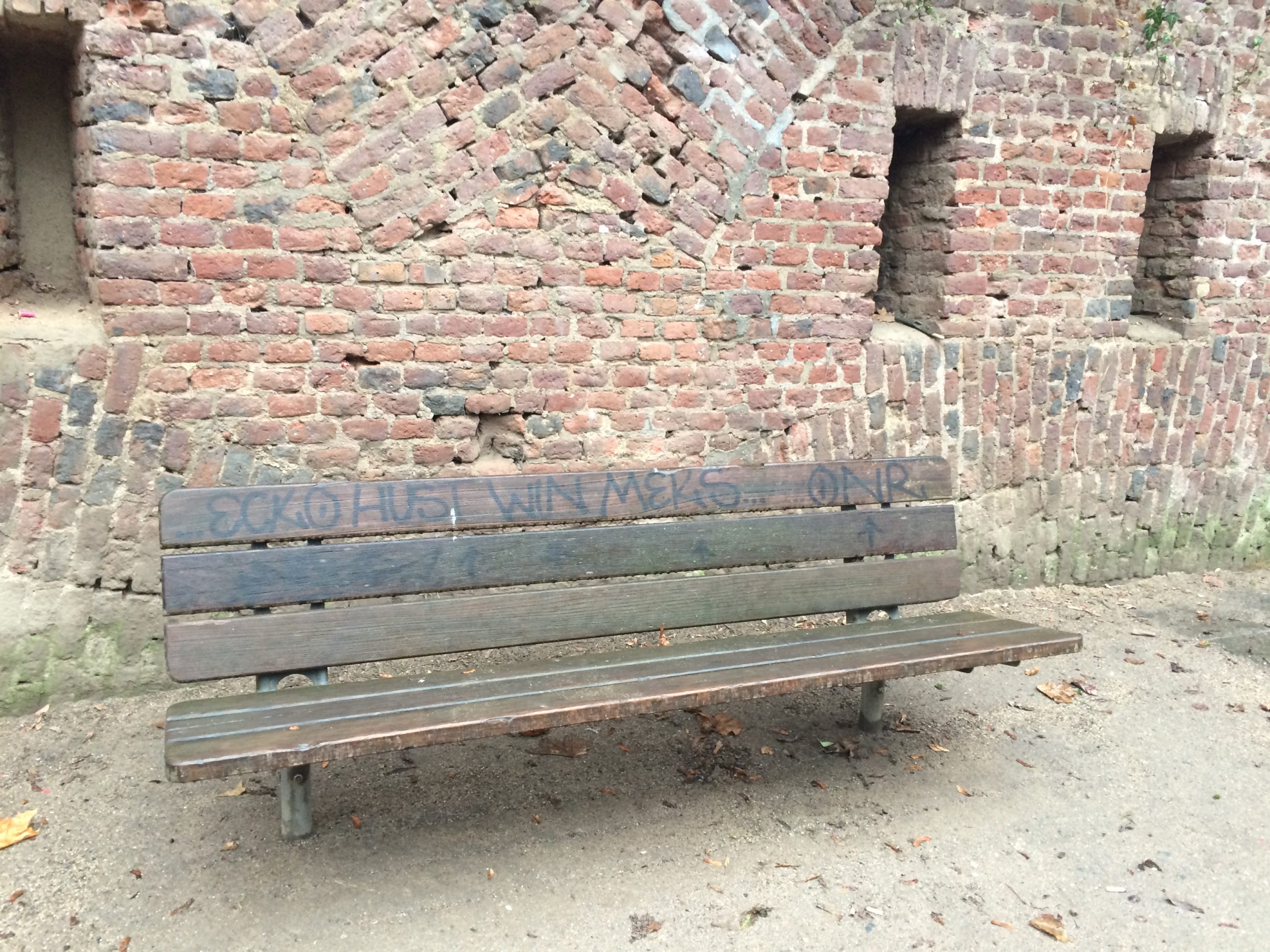 an empty park bench with graffiti scrawled on it in marker