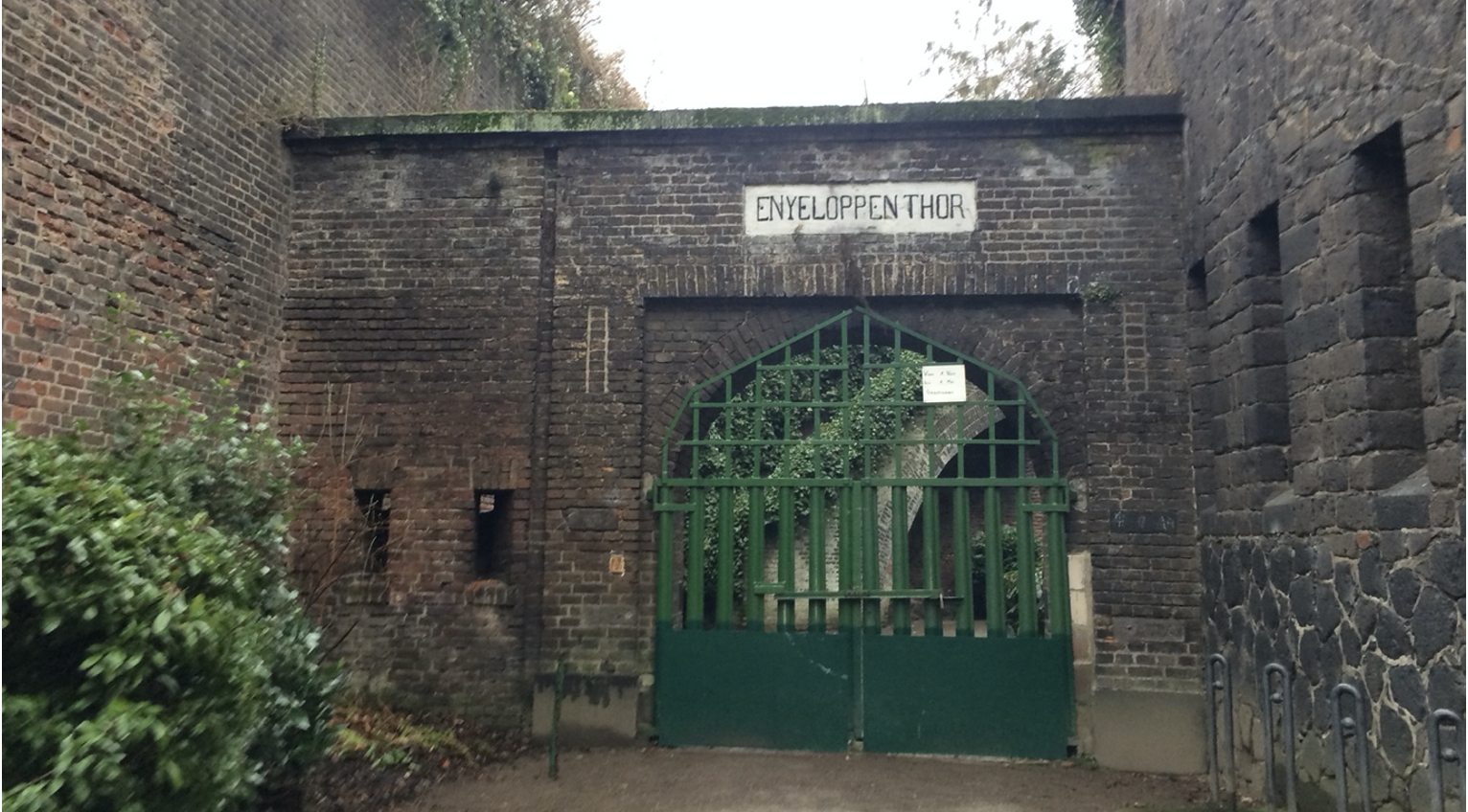 An arched green gate inset into a Medieval brick structure